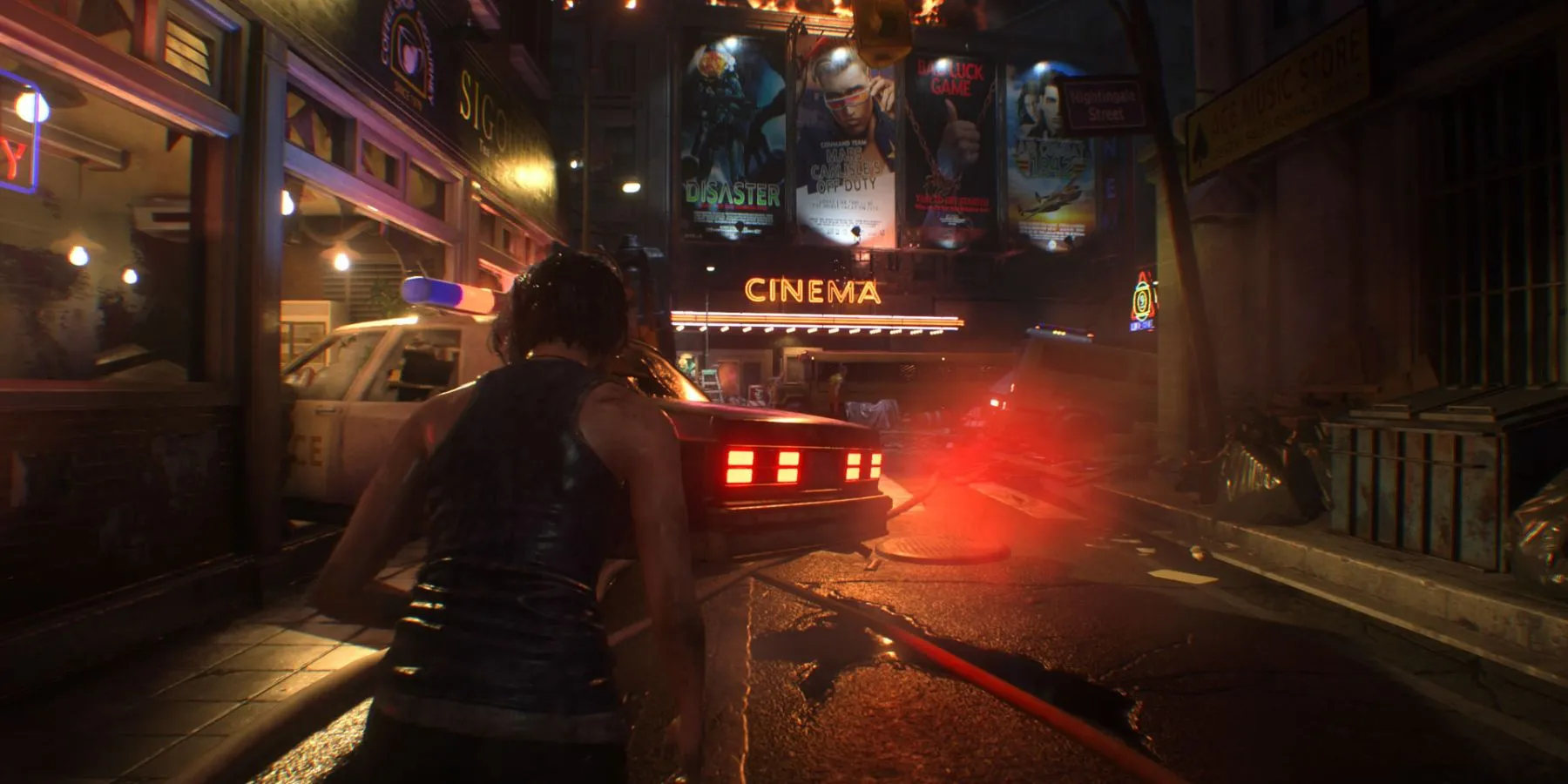 Jill Valentine trên một con phố cùng biển hiệu rạp chiếu phim và xe cảnh sát trong Resident Evil 3 Remake.